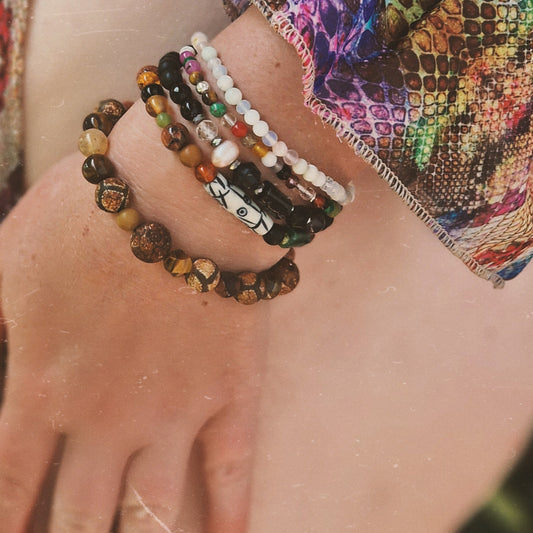 Close-up of a woman’s wrist adorned with the Anri Zenya Pearl & Crystal Whisper bracelet, featuring mother-of-pearl, agate, howlite, and clear quartz beads against a flowing silk dress