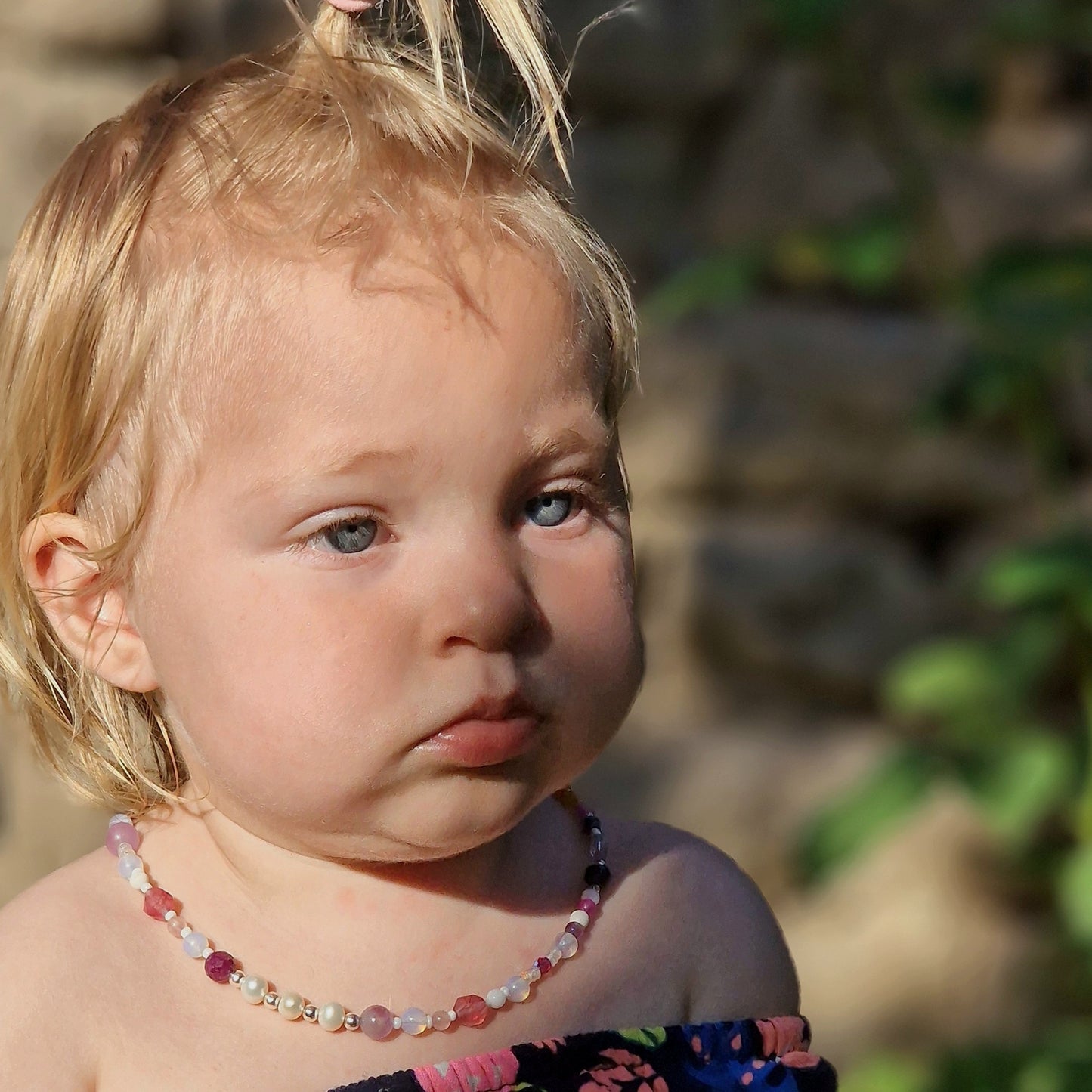 Little girl with golden hair and blue eyes in a meadow, her neck adorned with a beautiful ruby and pearl gemstone necklace