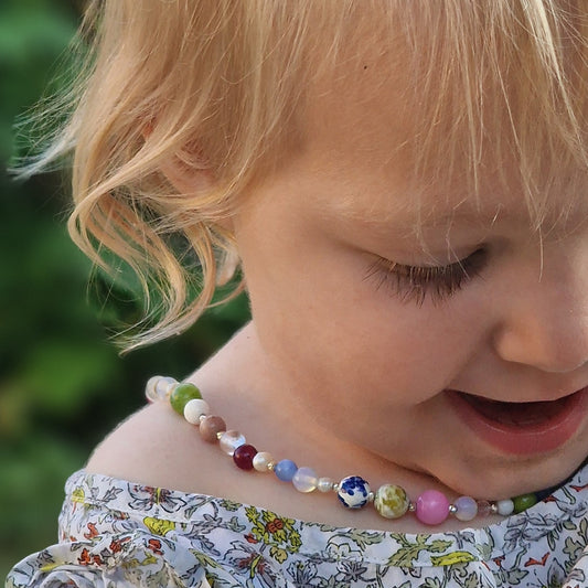 Young blonde girl with blue eyes wearing the gentle gemstone necklace, featuring mother-of-pearl, moonstone, agate, pearls, tourmaline, quartz, and andalusite