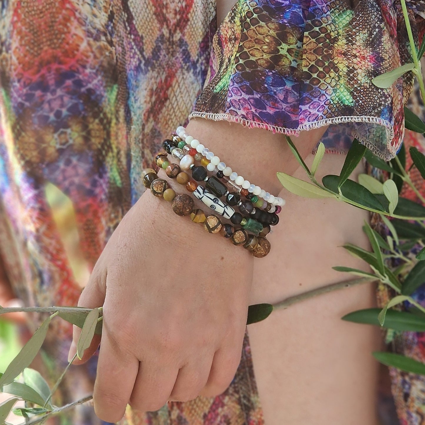 Close detail of the handcrafted elastic cord and sterling silver accents of the Anri Zenya set on a woman’s hand resting on lace fabric