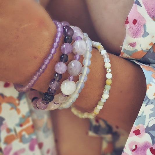 Stack of five gemstone bracelets on a woman’s wrist featuring jadeite, amethyst, Madagascar jade, moonstone, howlite, azurite and agate
