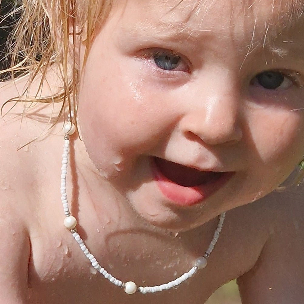 A young girl with blonde hair wearing a luxurious white pearl and Japanese bead necklace with a sterling silver clasp