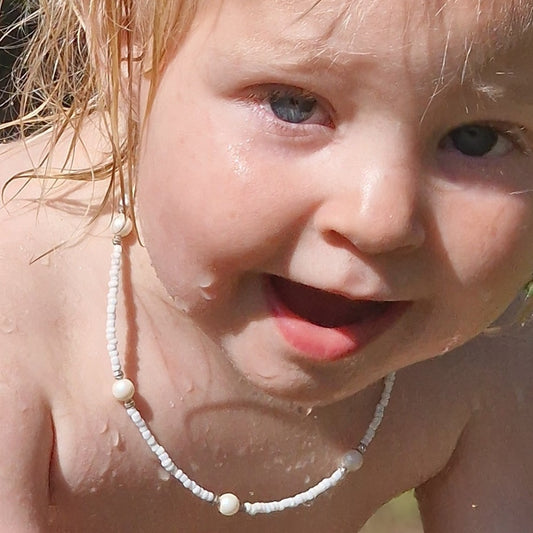 A young girl with blonde hair wearing a luxurious white pearl and Japanese bead necklace with a sterling silver clasp