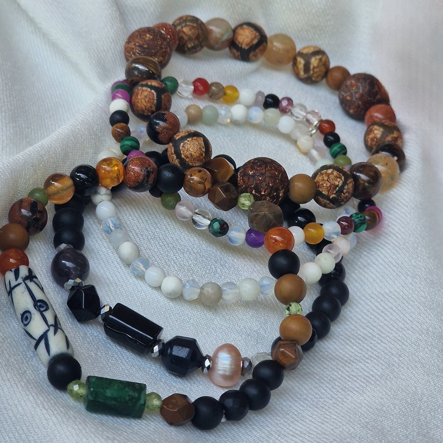 A stack of five Anri Zenya designer gemstone bracelets featuring pearl, agate, howlite, malachite, emerald, topaz, sapphire, tiger’s eye, sunstone and an African Lesotho charm on a neutral background