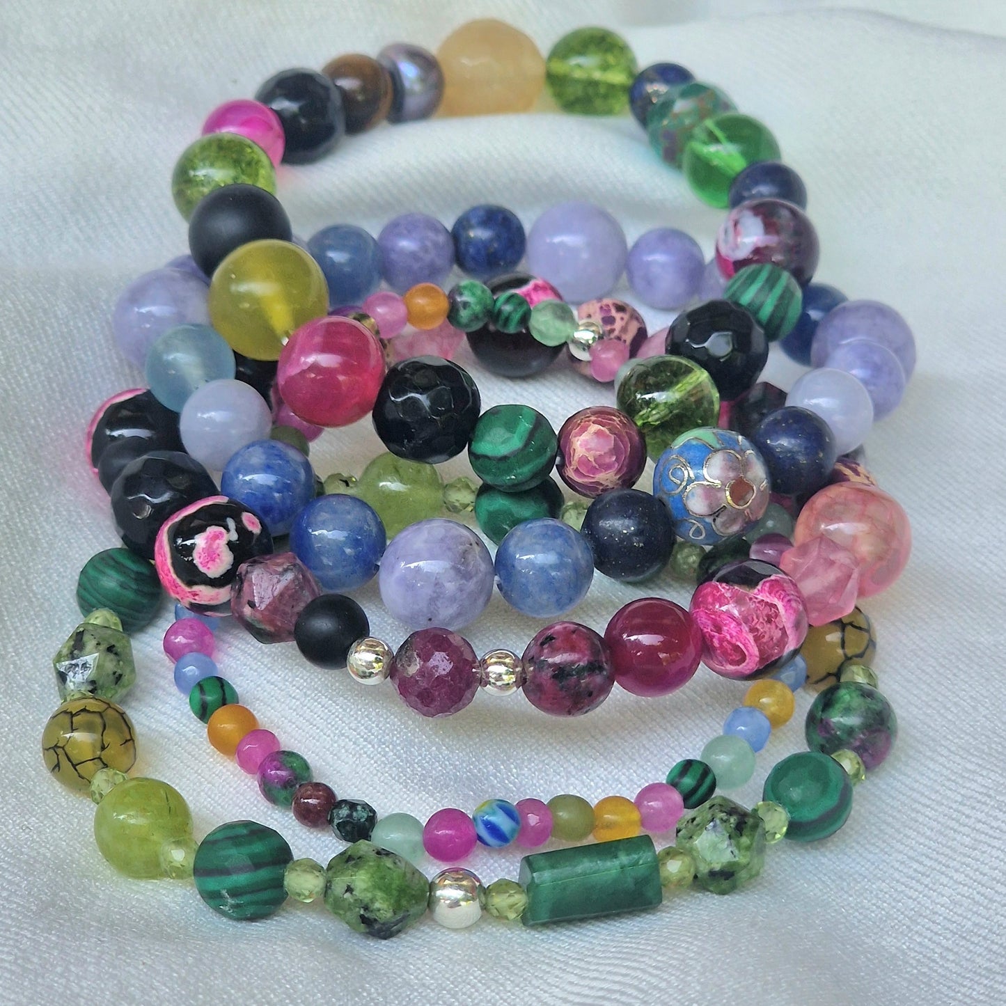 Elegant evening shot of the full Jenove Amante Zen designer bracelet collection layered on a slender wrist, each gemstone bracelet strung on elastic cord and accented with sterling silver