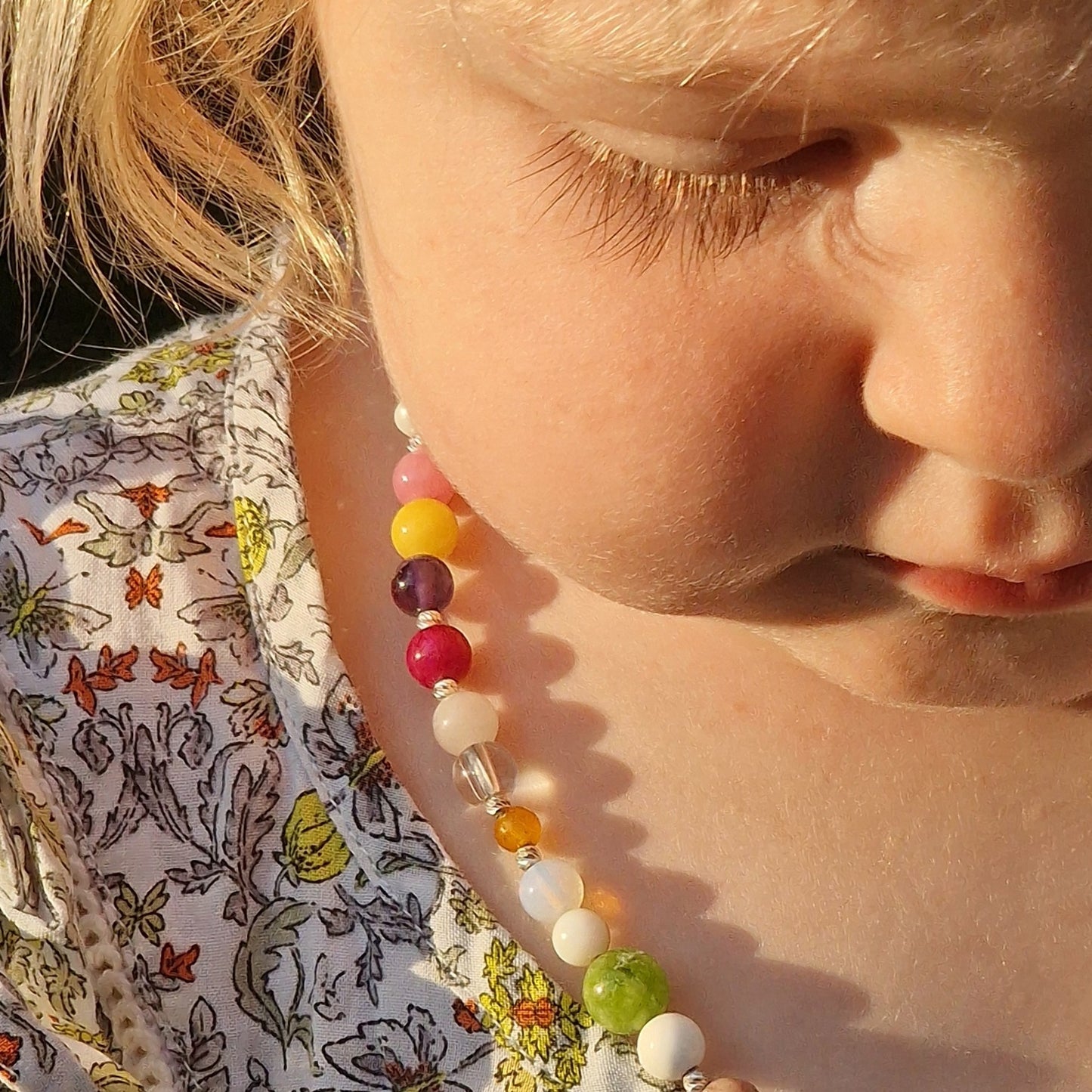 Portrait of a smiling little princess with blue eyes, her blonde hair framing the Limited Edition gemstone necklace with silver clasp